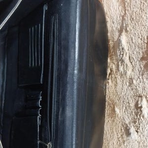 Puede incluir: Malet&iacute;n de cuero negro con m&uacute;ltiples compartimentos interiores, incluyendo un bolsillo con cremallera y ranuras para tarjetas. El malet&iacute;n est&aacute; abierto, revelando los detalles interiores. El cuero parece tener un ligero brillo.