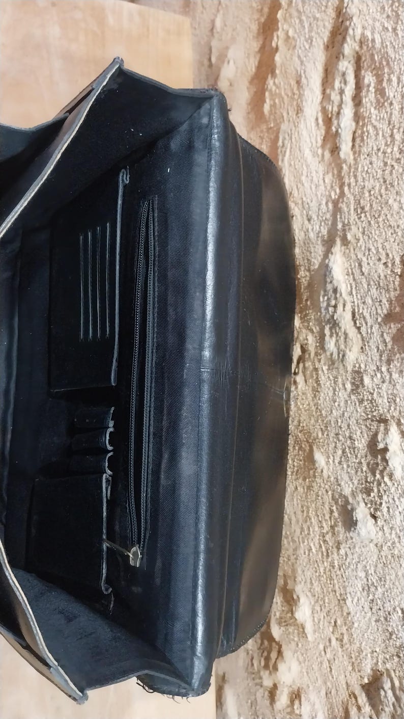 Puede incluir: Malet&iacute;n de cuero negro con m&uacute;ltiples compartimentos interiores, incluyendo un bolsillo con cremallera y ranuras para tarjetas. El malet&iacute;n est&aacute; abierto, revelando los detalles interiores. El cuero parece tener un ligero brillo.