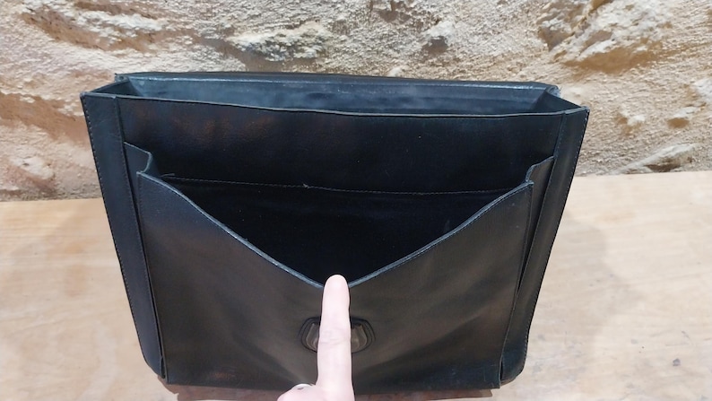 Puede incluir: Malet&iacute;n de cuero negro con interior abierto y m&uacute;ltiples bolsillos. La bolsa tiene forma rectangular con cierre de solapa y asa. El interior est&aacute; forrado con una tela oscura. El malet&iacute;n est&aacute; dise&ntilde;ado para transportar documentos y otros elementos esenciales.