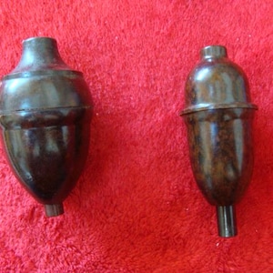 May include: Two vintage brown bakelite light fittings with a glossy finish. One is acorn-shaped, the other is more cylindrical. Both have a dark brown stem. The fittings are set against a red background.