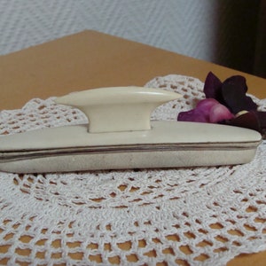 Peut inclure: Un polissoir à ongles blanc avec une poignée surélevée. Le polissoir est sur un napperon blanc en crochet.