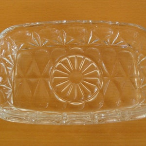 Peut inclure: Un plat rectangulaire en verre transparent avec un motif décoratif. Le plat a une partie centrale surélevée avec un motif circulaire.
