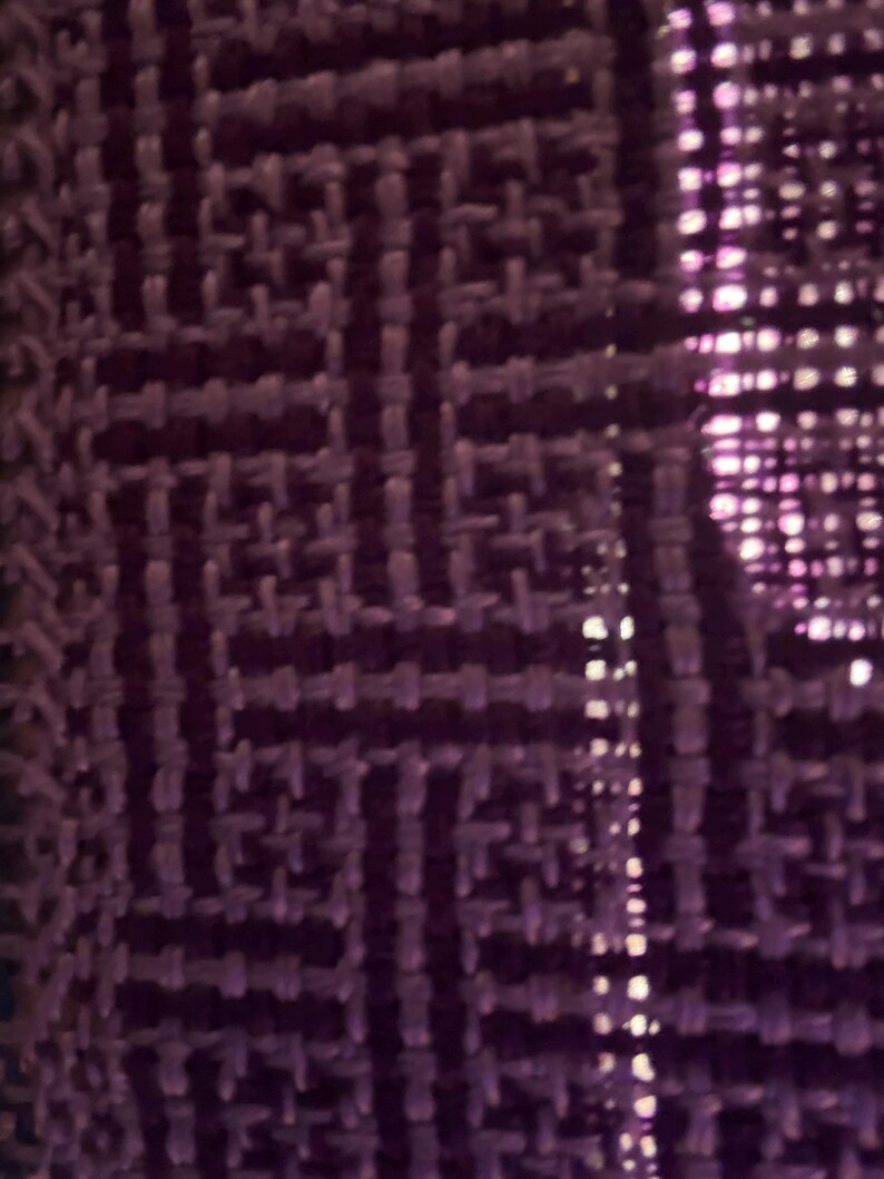 Puede incluir: Primer plano de una tela tejida con un patr&oacute;n geom&eacute;trico en tonos morados. La textura parece ser un tejido apretado, con un brillo sutil. El dise&ntilde;o presenta formas entrelazadas, creando una superficie texturizada.