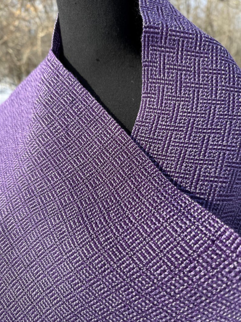 Puede incluir: Primer plano de una tela morada tejida con un patr&oacute;n de diamantes. La tela est&aacute; drapeada sobre una forma negra, mostrando la textura y las variaciones de color. El tejido crea una superficie texturizada.