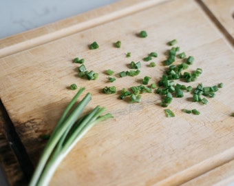 May include: A wooden cutting board with a bundle of green chives and chopped chives scattered across the surface.