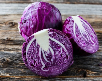 May include: Three red cabbages, one whole and two cut in half, on a rustic wooden surface. The cut cabbages reveal the white inner layers and purple outer layers.