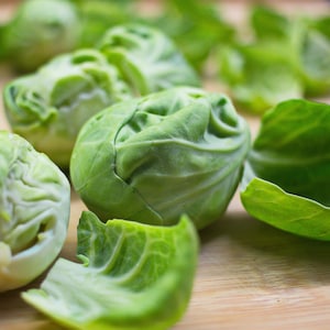 May include: A close-up of several green Brussels sprouts on a wooden surface. The sprouts are arranged in a cluster, with some of the leaves removed to reveal the inner part of the vegetable.