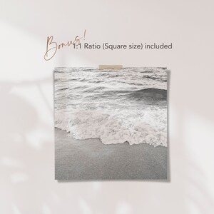May include: A black and white photograph of ocean waves crashing on a sandy beach. The image is a close-up of the waves and the sand.