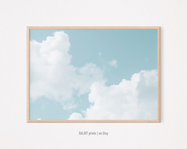 May include: A framed print of a light blue sky with white clouds. The frame is made of light wood.