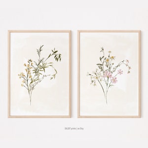 May include: Two framed prints of watercolour botanical illustrations. The print on the left features a bouquet of yellow and green wildflowers. The print on the right features a bouquet of white and pink wildflowers.