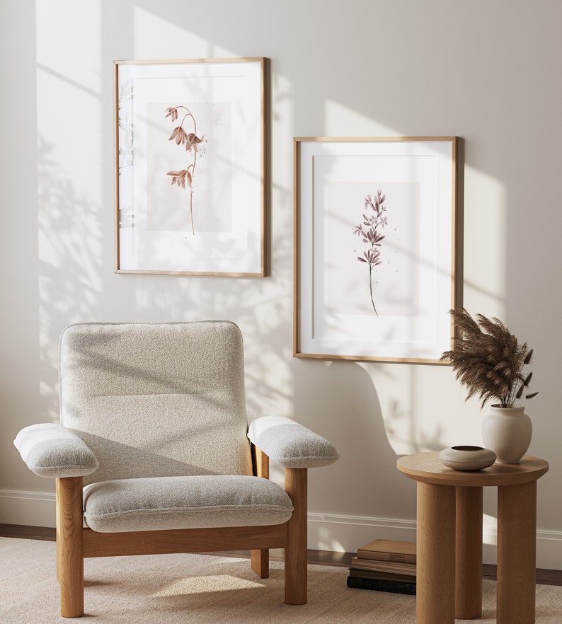 May include: Two framed botanical prints with delicate brown and purple flowers on a light background. The prints are hanging on a white wall with a beige armchair and a small wooden side table in the foreground.