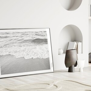 May include: A black and white photograph of ocean waves crashing on a sandy beach, framed in a black frame.