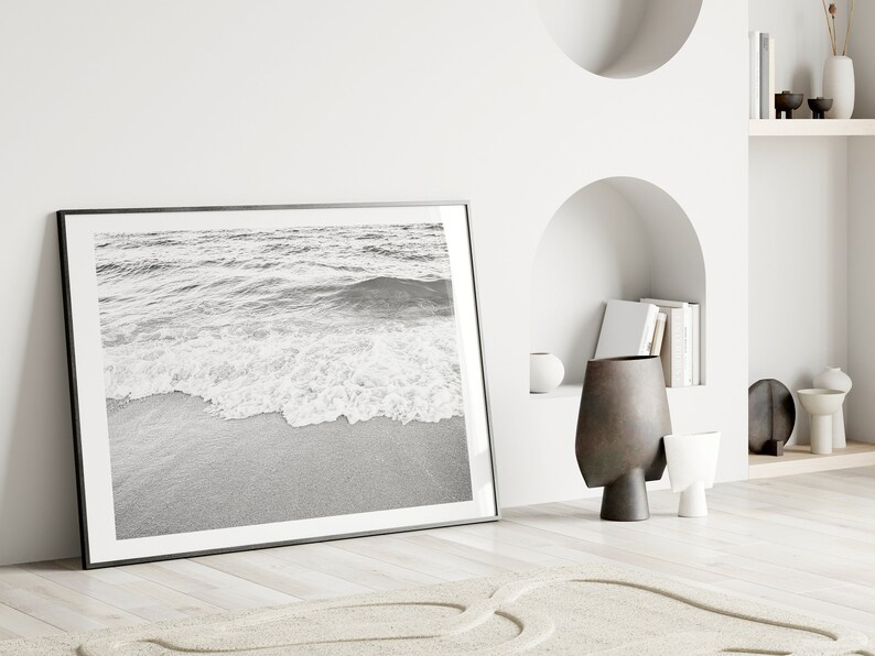 May include: A black and white photograph of ocean waves crashing on a sandy beach, framed in a black frame.