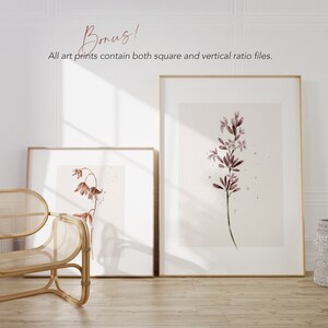 May include: Two framed watercolor prints of delicate pink flowers on a white background. The prints are in gold frames and are hanging on a white wall.
