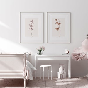 May include: Two framed watercolor prints of botanical illustrations. The print on the left features a pink flower with a brown stem. The print on the right features a brown flower with a brown stem. The prints are hanging on a white wall above a white desk with a white stool.
