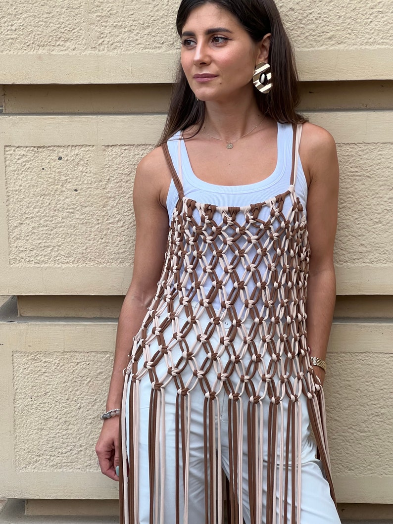May include: A brown and cream crocheted top with long fringe. The top is sleeveless and has a loose fit.