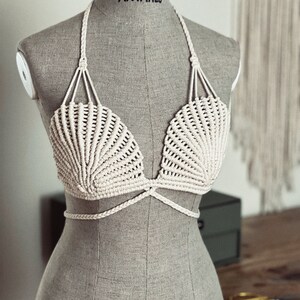 May include: A white crocheted bikini top with a shell-shaped design. The top has adjustable straps and a tie closure at the back.
