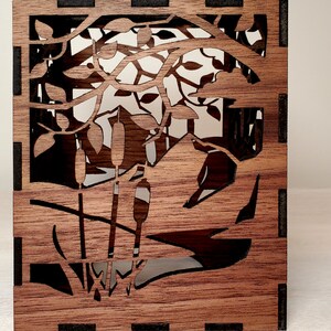 May include: A wooden box with a laser-cut design of cattails and reeds in a pond. The box is made of dark brown wood with black accents.