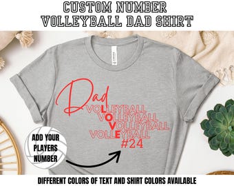 May include: A heather gray t-shirt with the words "Dad Volleyball" in red script. The shirt includes the text "Add Your Players Number" and "#24". The shirt is a custom volleyball dad shirt.