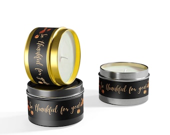 May include: Three small candle jars with black labels and gold lettering that reads "So thankful for you!" The candles are in different stages of burning. The jars are on a white surface.