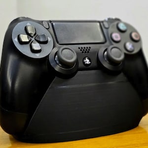 Pode incluir: Um controlador PlayStation 4 preto com uma pega texturizada e uma base preta. O controlador tem um layout padrão com botões, joysticks e um touchpad.