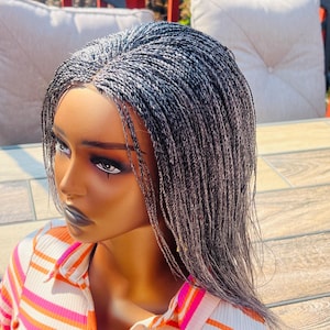 May include: A mannequin head with a gray braided wig. The wig features a natural hairline and is styled in small, individual braids. The mannequin is wearing a striped shirt with pink, orange, and white stripes.