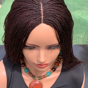 May include: A dark brown wig with small braids, styled in a long, straight, and flowing style. The wig is made with synthetic hair and has a lace front.