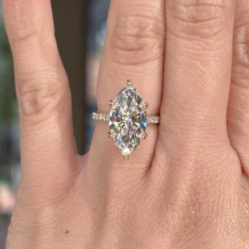 May include: A marquise-cut diamond engagement ring. The large, clear diamond is set in a gold band with smaller diamonds on the sides. The ring is on a person's finger.