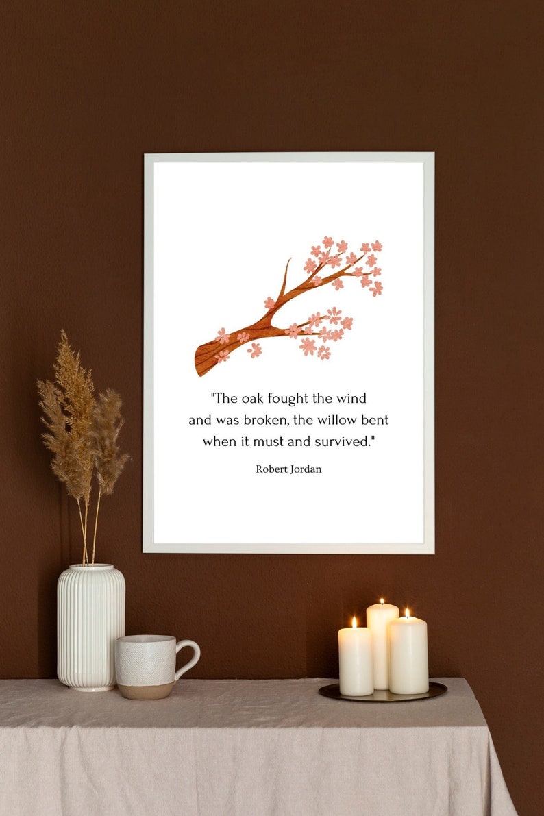 May include: A white framed print with a pink and brown illustration of a tree branch with pink flowers. The print features a quote by Robert Jordan: "The oak fought the wind and was broken, the willow bent when it must and survived."