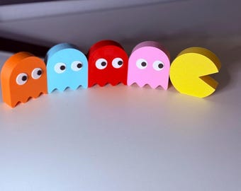 May include: A collection of colorful wooden Pac-Man ghosts and Pac-Man. The ghosts are orange, blue, red, and pink, each with white eyes. The Pac-Man is yellow with a mouth open. A fun, retro gaming theme.