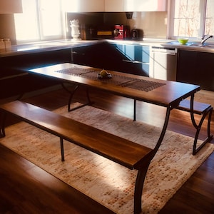 May include: A wooden table with two benches, set in a kitchen with black cabinets and a rug. Three black pendant lights hang over the table.