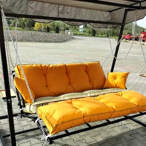 May include: A black metal swing set with a yellow cushioned seat and a gray canopy. The swing set is outdoors on a paved surface.