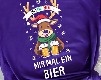 Könnte beinhalten: Ein lila T-Shirt mit einem Cartoon-Rentier, das einen Weihnachtsmannhut und einen Schal trägt und zwei Bierkrüge hält. Der Text "HO HO HOL" steht über dem Rentier, und "MIR MAL EIN BIER" steht darunter. Schneeflocken sind verstreut.