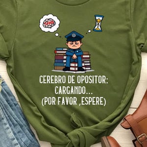 Könnte beinhalten: Olivgrünes T-Shirt mit einer Grafik eines Polizisten, der auf Büchern sitzt, mit Gedankenblasen eines Gehirns und einer Sanduhr. Der Text auf dem Shirt lautet "Cerebro de Opositor: Cargando... (Por Favor, Espere)". Braune Stiefeletten und zerrissene blaue Jeans.