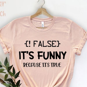 May include: A peach-coloured t-shirt with black text that reads "{!FALSE} IT'S FUNNY BECAUSE IT'S TRUE".