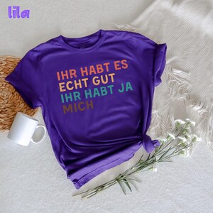 May include: Purple short-sleeved t-shirt with the text "Ihr habt es echt gut ihr habt ja mich" in rainbow colors.
