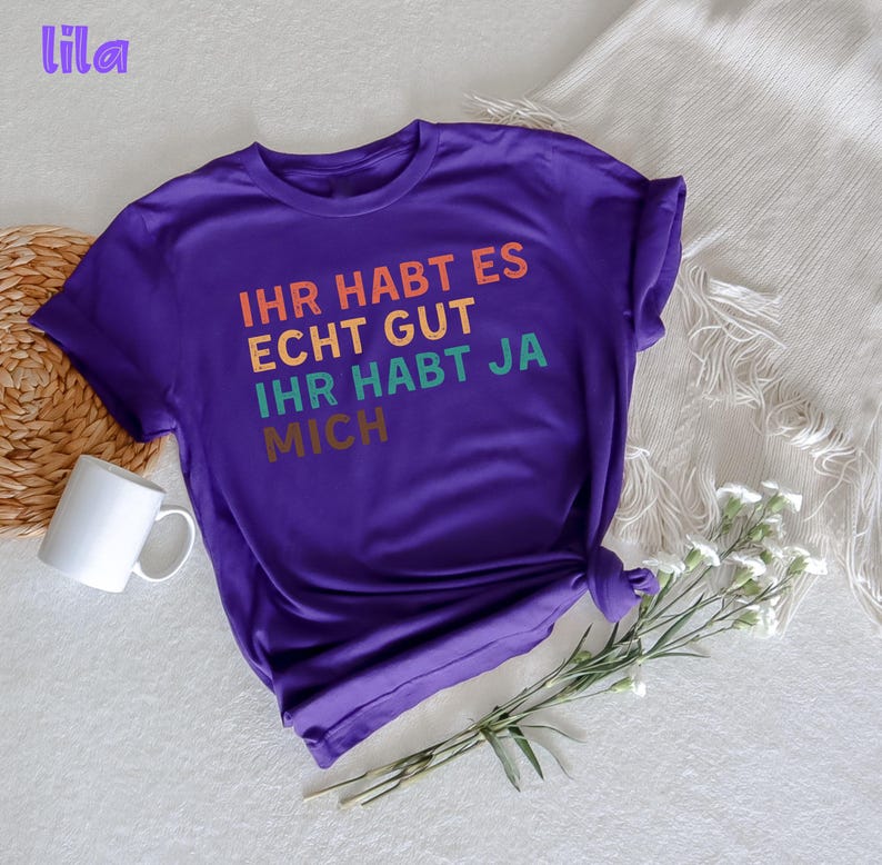 May include: Purple short-sleeved t-shirt with the text "Ihr habt es echt gut ihr habt ja mich" in rainbow colors.