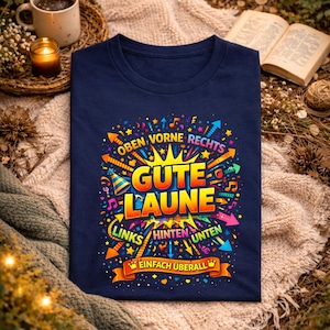 May include: A navy blue t-shirt with a colorful graphic design. The design includes the words "Gute Laune" in large yellow letters, surrounded by arrows, musical notes, and other decorative elements. The word "marine" is at the top.