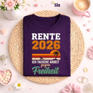 May include: A purple t-shirt with the text "RENTE 2026" in white and orange. Below the text is a sunset graphic with a palm tree. The text "ICH TAUSCHE ARBEIT gegen Freiheit" is below the sunset graphic.