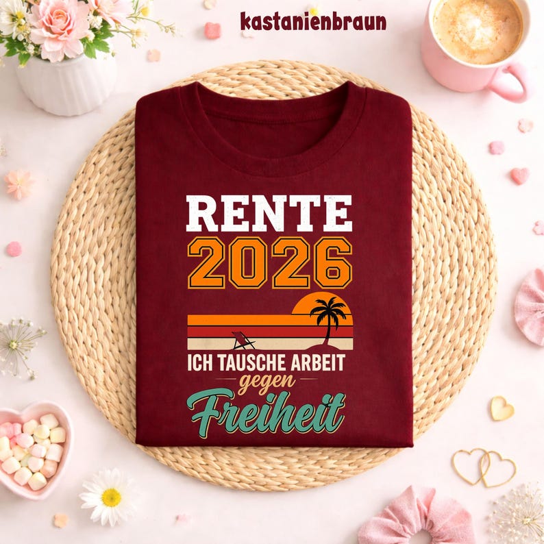 May include: A maroon t-shirt with the text "RENTE 2026" in white and orange, along with the phrase "ICH TAUSCHE ARBEIT gegen Freiheit" and a sunset graphic. The shirt is displayed on a woven mat.