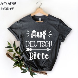 May include: Dark grey heather t-shirt with white text that reads "Auf Deutsch Bitte" with an arrow pointing to the right.
