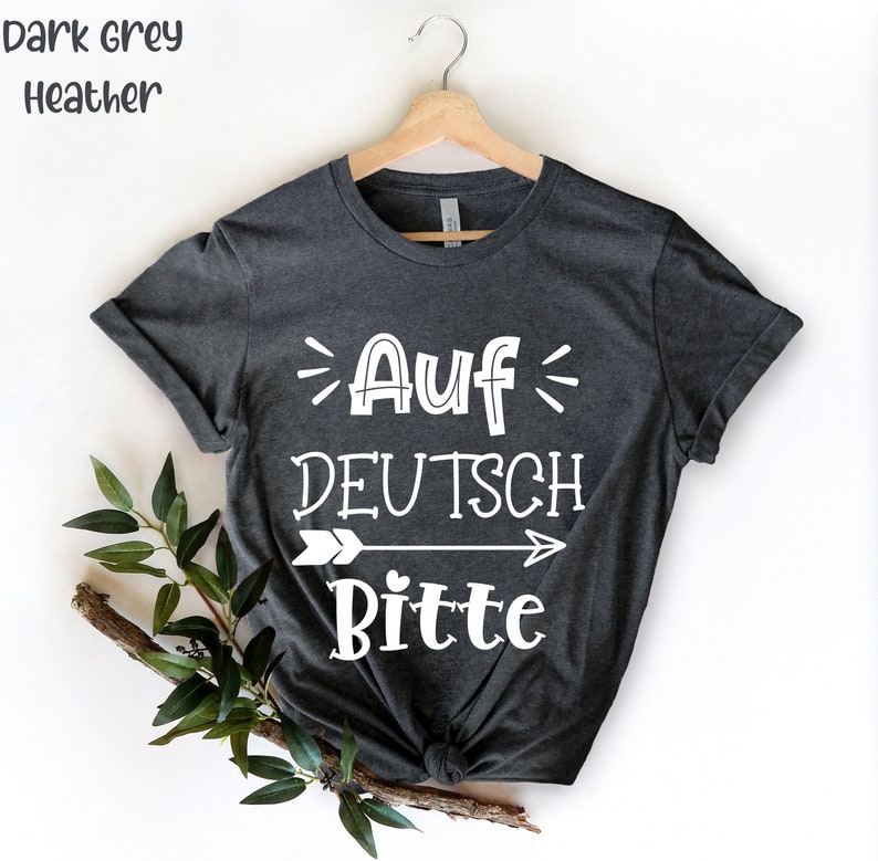 May include: Dark grey heather t-shirt with white text that reads "Auf Deutsch Bitte" with an arrow pointing to the right.