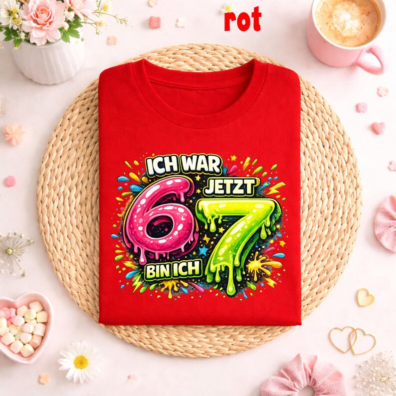 Peut inclure: Un t-shirt rouge avec le texte allemand "ICH WAR 6, JETZT BIN ICH 7" et des graphismes color&eacute;s. Les chiffres 6 et 7 sont affich&eacute;s en rose et vert. Le mot "rot" est &eacute;crit en rouge en haut.