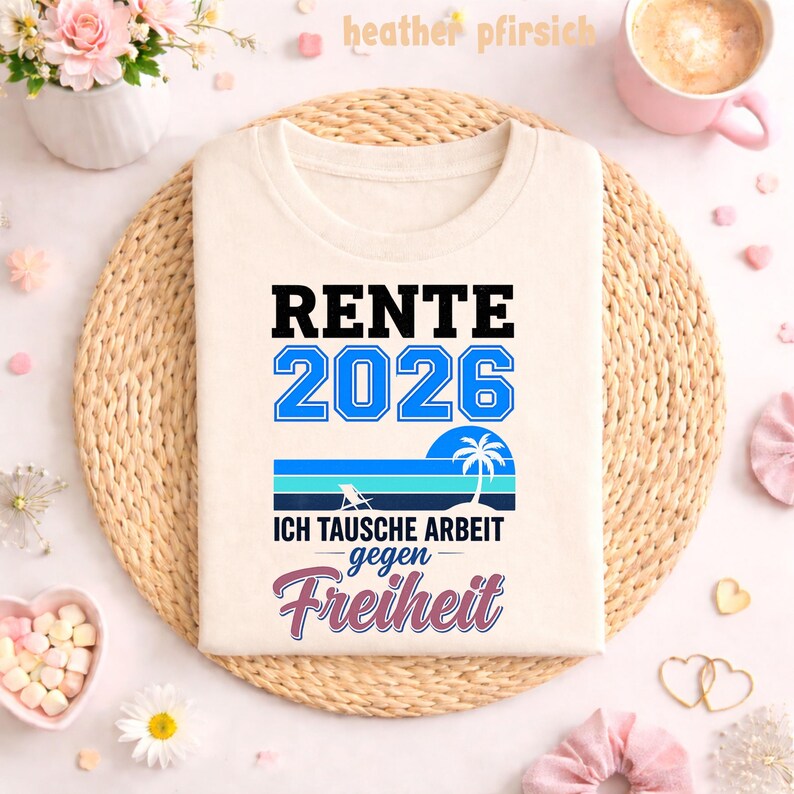 May include: Cream-colored t-shirt with the text "RENTE 2026" in black and blue. Below, a graphic of a beach scene with a palm tree and the words "ICH TAUSCHE ARBEIT gegen Freiheit" in blue and pink. The shirt is displayed on a woven mat.