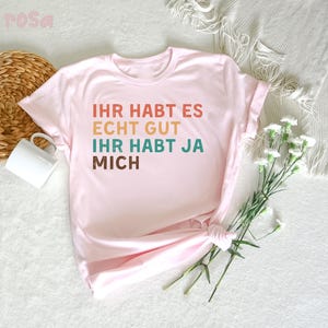May include: Pink t-shirt with the text "Ihr habt es echt gut ihr habt ja mich" in rainbow colors.