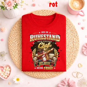 May include: A red crew neck t-shirt with the German text "BIN IM RUHESTAND MEIN EINZIGER Chef IST JETZT MEINE FRAU!" and a graphic of a man dabbing. The graphic includes a man in a hat and plaid shirt sitting on a couch.