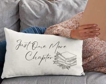 May include: A white throw pillow with the text "Just One More Chapter" and a black and white illustration of a stack of books with leaves. The pillow is on a gray couch.