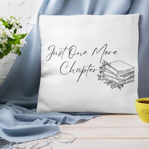 May include: White throw pillow with black text that reads "Just One More Chapter" and a black and white illustration of a stack of books with flowers.