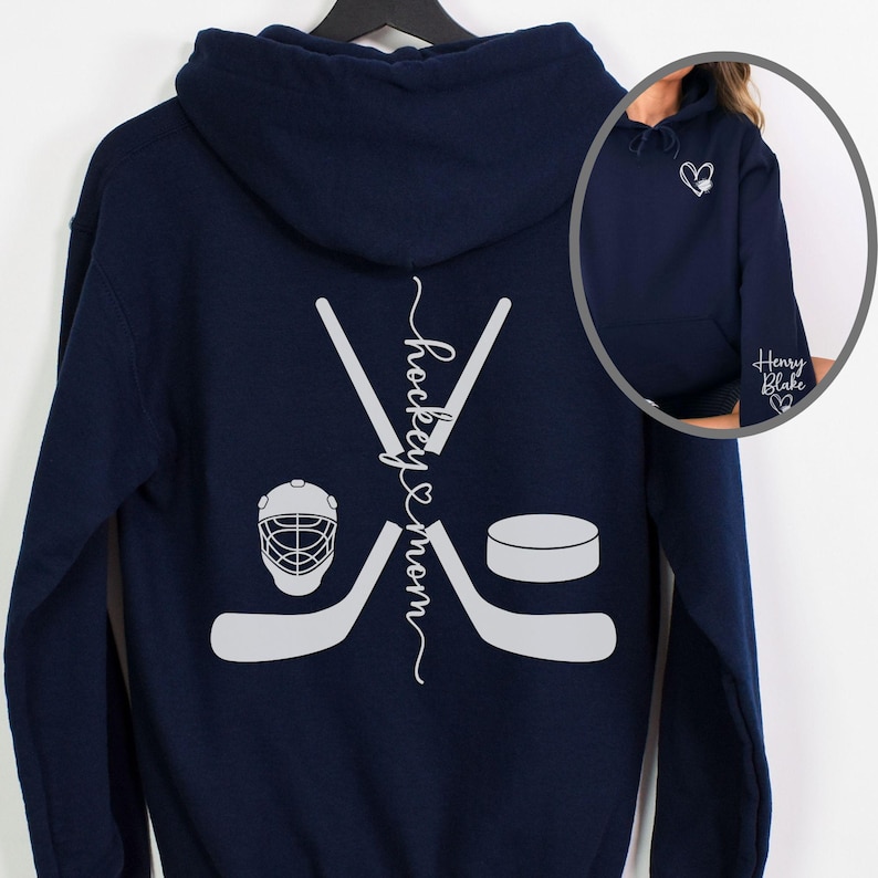 K&ouml;nnte beinhalten: Marineblauer Hoodie mit einem wei&szlig;en Hockeyschl&auml;ger- und Puck-Design auf der R&uuml;ckseite. Der Text "hockey & mom" ist vertikal auf der R&uuml;ckseite des Hoodies geschrieben.