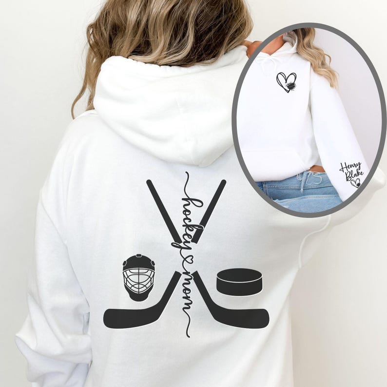 K&ouml;nnte beinhalten: Wei&szlig;er Hoodie mit einem schwarzen Hockey-Schl&auml;ger- und Puck-Design auf der R&uuml;ckseite. Der Text "hockey & mom" ist vertikal auf der R&uuml;ckseite des Hoodies geschrieben. Die Vorderseite des Hoodies hat ein kleines schwarzes Herz mit einem Hockeyschl&auml;ger darin.